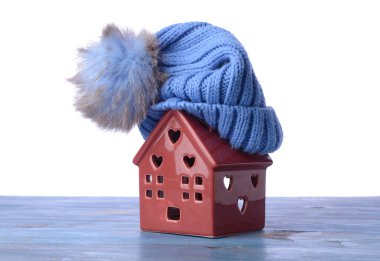 Beyaz arka planda masa üzerinde ev ve sıcak şapka figürü. Isınma mevsimi kavramı