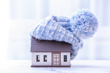 Masanın üzerinde ev ve sıcak şapka figürü. Isınma mevsimi kavramı