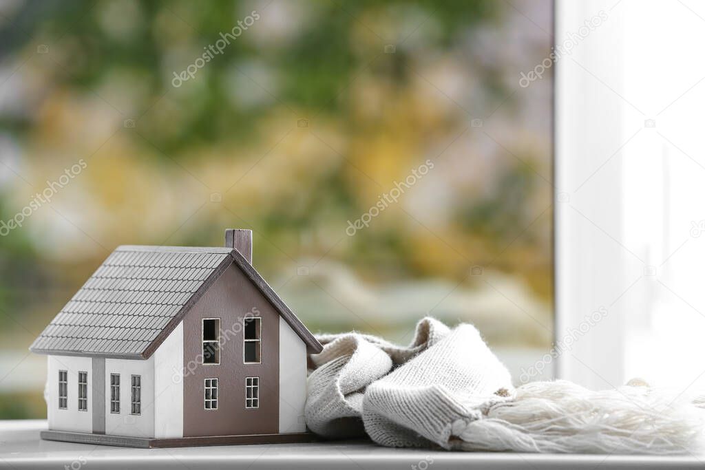 Figure of house and warm scarf on window sill. Concept of heating season