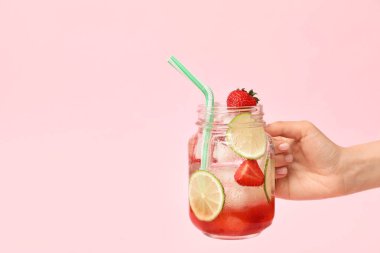 Arka planda taze çilekli limonata kavanozu olan bir kadın eli.