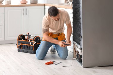 Mutfaktaki buzdolabını tamir eden bir işçi.