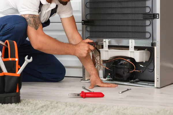 Worker repairing fridge in kitchen