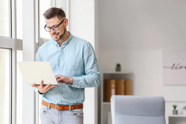 Portrait of male psychologist with laptop near window in office