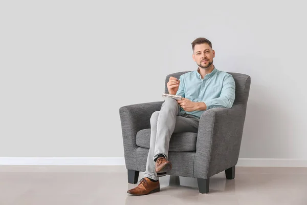 Male psychologist sitting in armchair near light wall