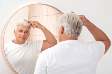 Kıdemli adam aynanın yanında saçını tarıyor.