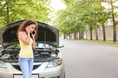 Stresli Afro-Amerikalı kadın dışarıda bozuk arabanın yanında telefonla konuşuyor.