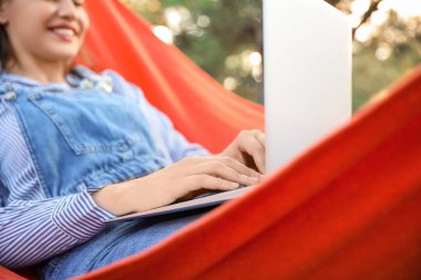 Diz üstü bilgisayarı olan, dışarıda hamakta dinlenen güzel genç bir kadın.