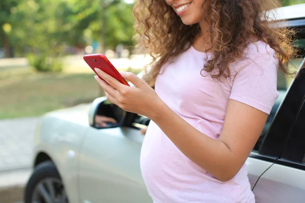 妊娠中のアフリカ系アメリカ人女性屋外で車の近くの携帯電話と — ストック写真