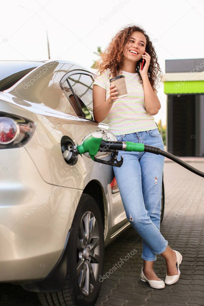 African-American woman talking by phone while filling up car tank at gas station