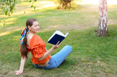 Parkta dinlenirken kitap okuyan güzel genç bir kadın.