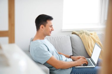 Evde dizüstü bilgisayarda çalışan genç adam.