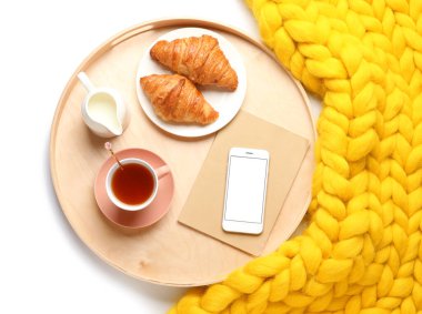Lezzetli kahvaltı tepsisi, cep telefonu ve beyaz arka planda örülmüş ekose.