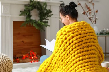 Evinde sıcak ekose kitap okuyan güzel genç bir kadın.