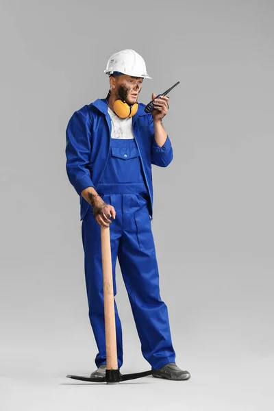 Miner man with pick axe and two-way radio on grey background