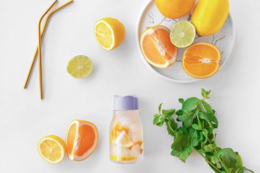 Beyaz zemin üzerinde sitruslarla doldurulmuş bir şişe nane suyu