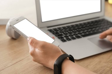 Laptop ve cep telefonuyla çalışan bir kadın ahşap masada, yakın plan.