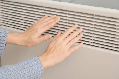 Radyatörde elini ısıtan kadın. Isınma mevsimi kavramı