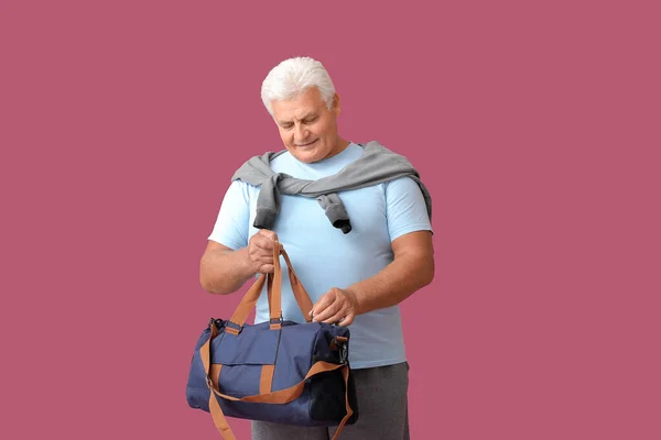 Sporty senior man with bag on color background