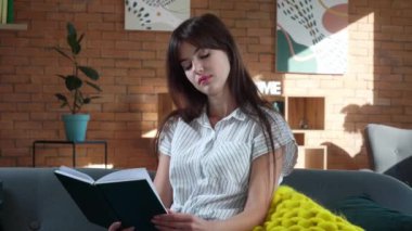 Evinde sıcak ekose kitap okuyan mutlu genç bir kadın.