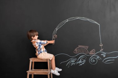 Siyah duvarın yanında elinde olta olan şirin bir çocuk.