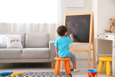 Anaokulunda tahtaya resim çizen şirin bir çocuk.