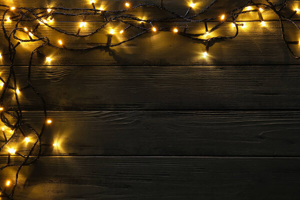 Glowing Christmas lights on dark wooden background