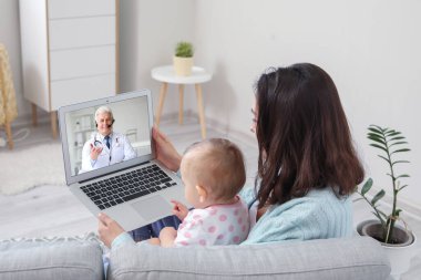 Young woman with her baby getting online consultation at home clipart