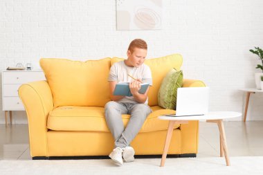 Evdeki kanepede oturan genç çocuk ödev yapıyor.