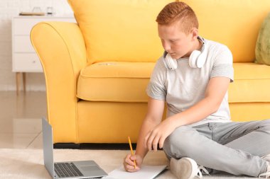 Genç çocuk ödevini yapıyor. Evde yerde oturuyor.