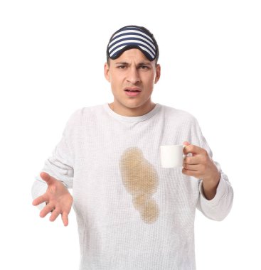 Beyaz arka planda pijamasında kahve lekeleri olan stresli genç bir adam.