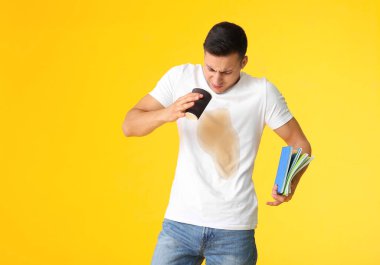 Tişörtünde kahve lekeleri olan stresli genç bir adam elinde renk arkaplanı üzerine not defterleri tutuyordu.