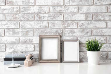 Boş fotoğraf çerçeveleri ve tuğla duvarın yanındaki masada bitkiler.