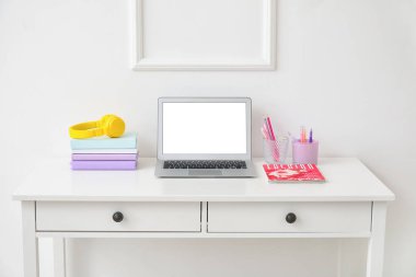 Beyaz duvarın yanında dizüstü bilgisayarı ve kulaklığı olan şık bir iş yeri.