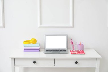 Beyaz duvarın yanında dizüstü bilgisayarı ve kulaklığı olan şık bir iş yeri.