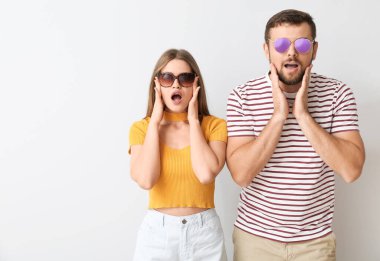 Işık arka planında şık güneş gözlüklü sürpriz bir çift.