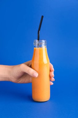 Renkli balkabağı smoothie şişesiyle kadın eli.
