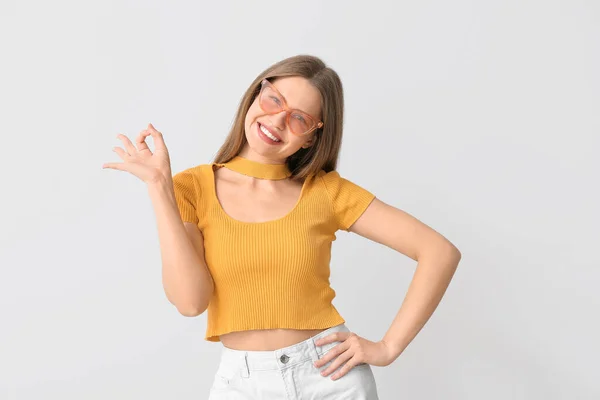 Schöne Frau Mit Stylischer Sonnenbrille Zeigt Geste Auf Hellem Hintergrund — Stockfoto