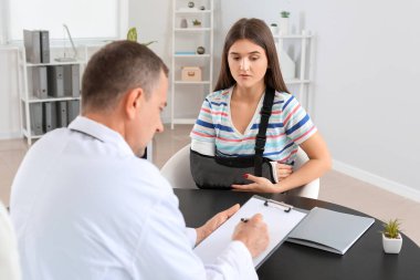 Kol kırığı olan genç bir kadın klinikte doktoru ziyaret ediyor.