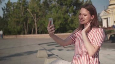 Cep telefonlu güzel genç bir kadın dışarıda selfie çekiyor.