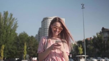 Dışarıda güneş gözlüğü takan, cep telefonlu güzel genç bir kadın.