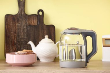 Elektrik ısıtıcısı, çaydanlık ve pasta mutfak masasında.