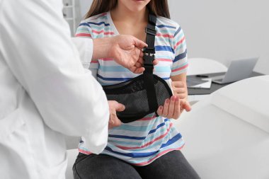 Kol kırığı olan genç bir kadın klinikte doktoru ziyaret ediyor.