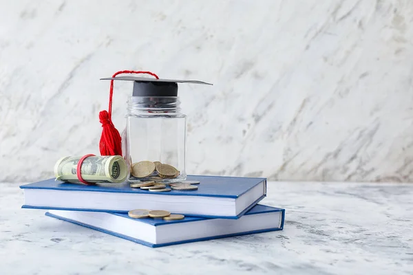 Graduation hat, books and jar with money on table. Tuition fees concept