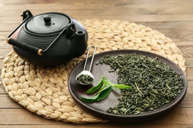 Çaydanlık ve kuru yeşil çay tabakta ahşap masada.