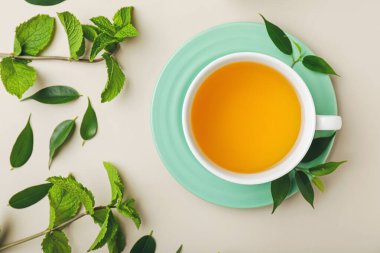 Bir fincan çay, arkaplanda nane ve yeşil yapraklar