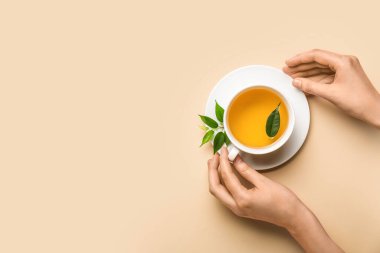 Kadın eli ve arka planda bir fincan sıcak aromatik çay.