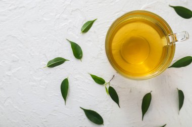 Bir fincan sıcak aromatik çay ve yeşil çay yaprakları.