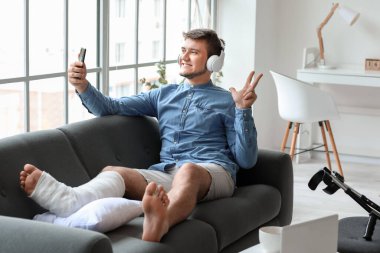 Kırık bacaklı genç adam evde müzik dinlerken selfie çekiyor.
