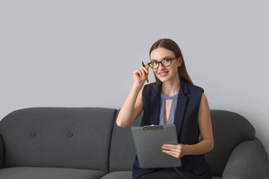 Kadın psikolog portresi gri arka planda koltukta oturuyor.