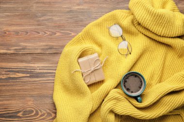 Noel hediyeli şık bir süveter, ahşap arka planda bir fincan kahve ve gözlük.